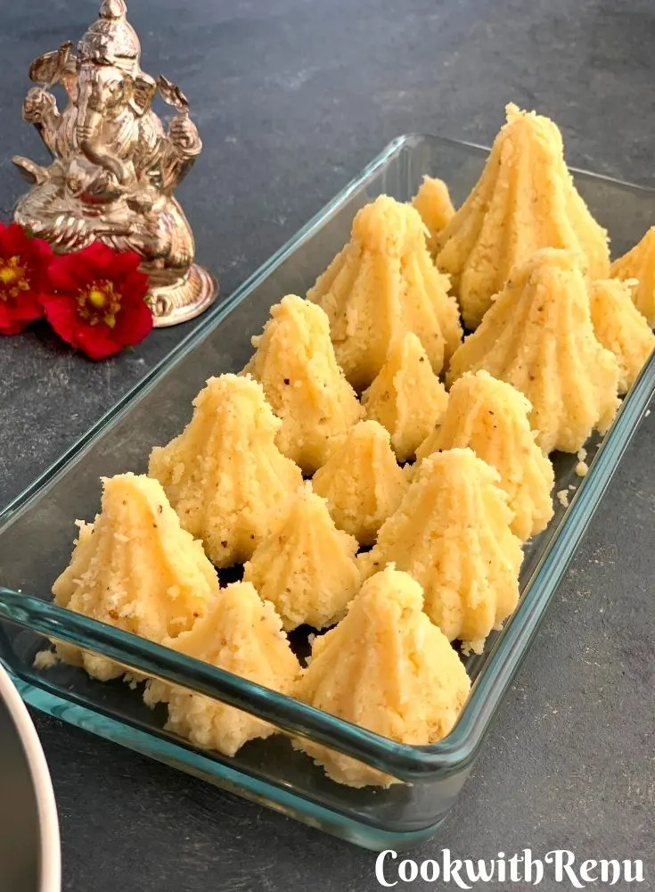 Microwave Condensed Milk Modak arranged on a rectangular glass tray. Seen along side is a statue of Lord Ganesha.
