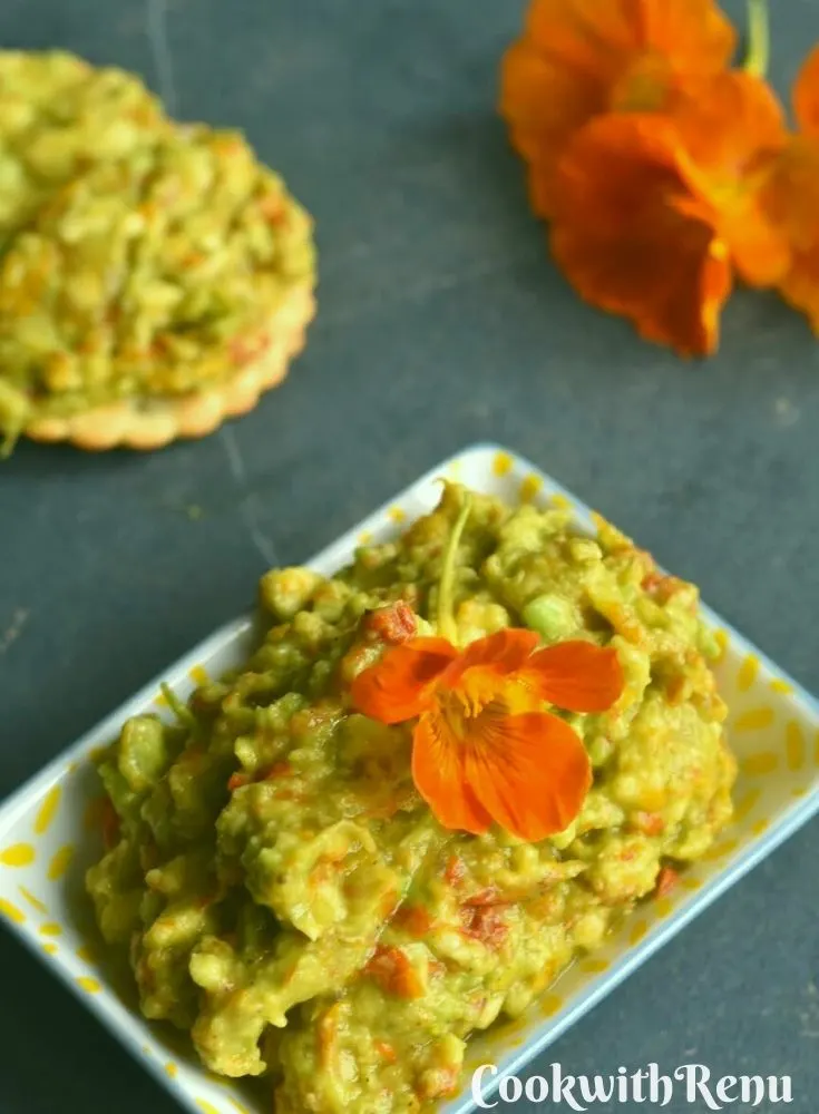 Close up look of Nasturtium Blossoms Avocado Guacamole with some nasturtium flowers and crackers on the side.