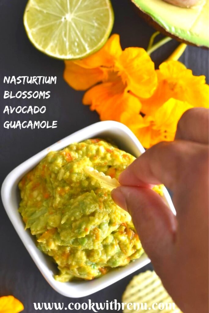 Nasturtium Blossoms Avocado Guacamole in a white square bowl, being enjoyed with chips. Seen along are some flowers, lemon.