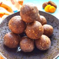 Ragi ladoos arranged as a pyramid in a black bowl. Seen along are some apricots and figs.