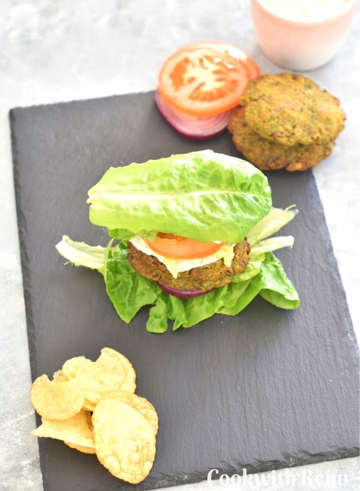 Top view of Vegan and Gluten-Free Pumpkin Chickpea Swiss Chard patties served on a black cheese board along with some potato crisp, onion, tomato, some more patties and nasturtium dip