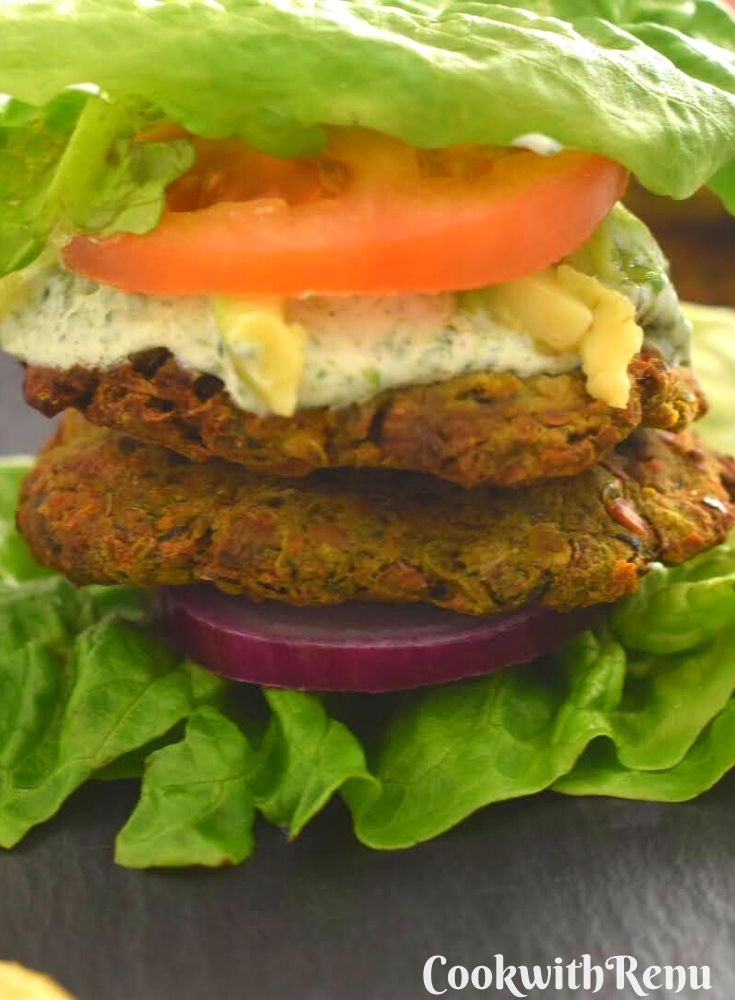 A close up look of Veggie chickpea patties served on a lettuce , with layers of onion, nasturtium dip, avocado and tomato