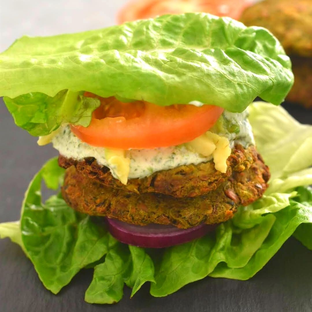 A close up look of Veggie chickpea patties served on a lettuce , with layers of onion, nasturtium dip, avocado and tomato