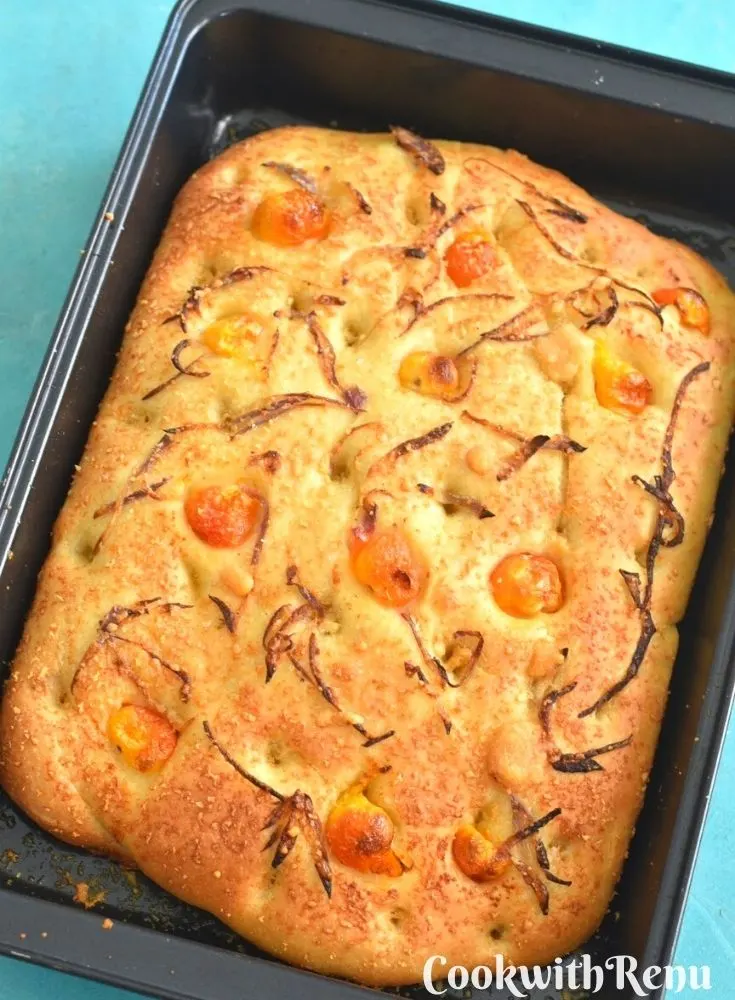 Focaccia bread with tomatoes and onions on a black baking tray