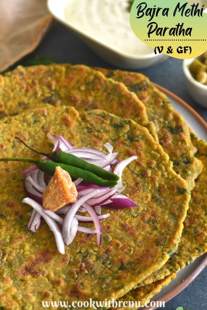 Bajra Methi Paratha served on a plate, with some cut onion, green chillies and jaggery.