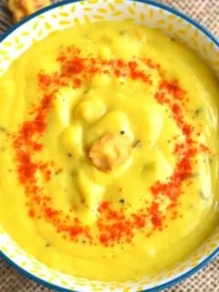Close up look of Mangodi Ki Kadhi served in a yellow bowl. A garnish of red chilly powder and some mangodi on top.