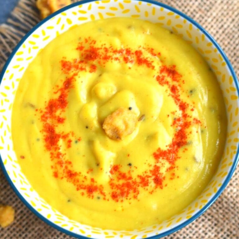Close up look of Mangodi Ki Kadhi served in a yellow bowl. A garnish of red chilly powder and some mangodi on top.