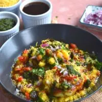 Ragda Pattice served in a black plate with a generous garnish of chutney, tomato, onion and sev