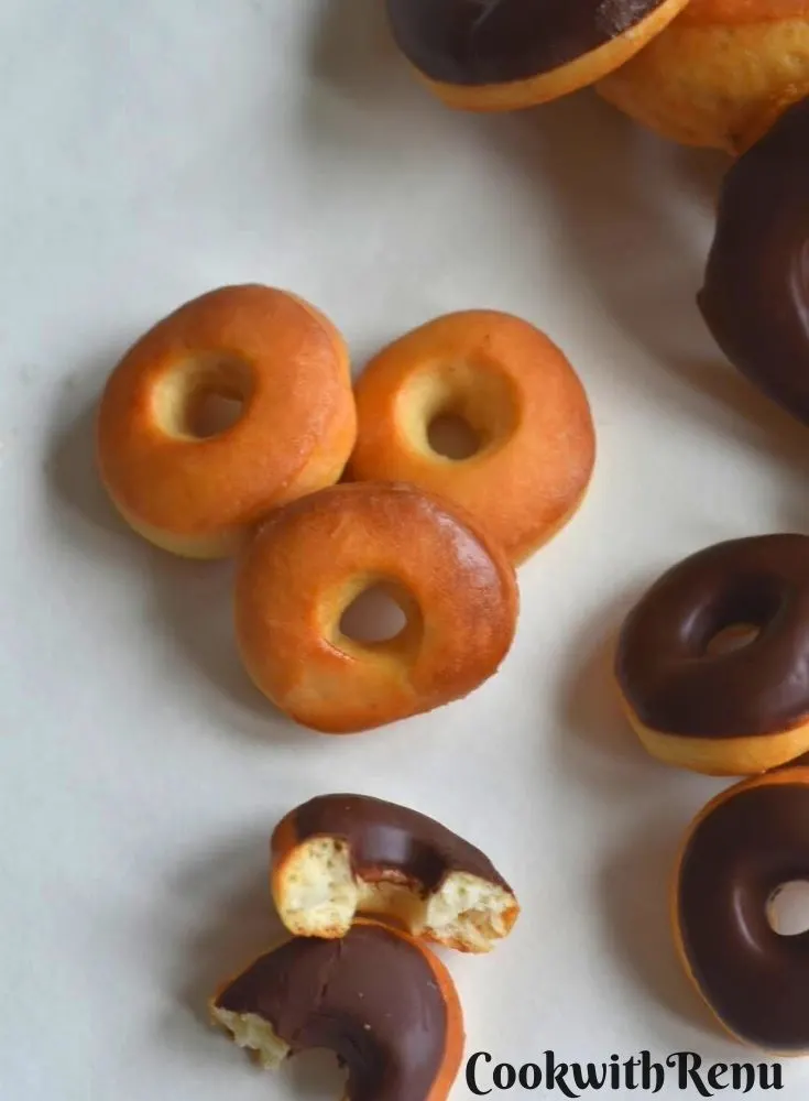 Sugar glazed donuts with some chocolate doughnuts on the side on a parchment paper