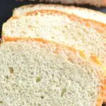 Slices of white bread arranged on a black cheese board with half cut bread seen in the background