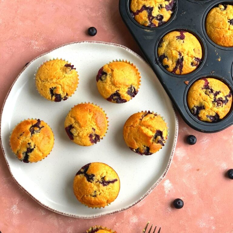 Blueberry Cornmeal Muffins arranged on a white plate with some blueberries scattered around