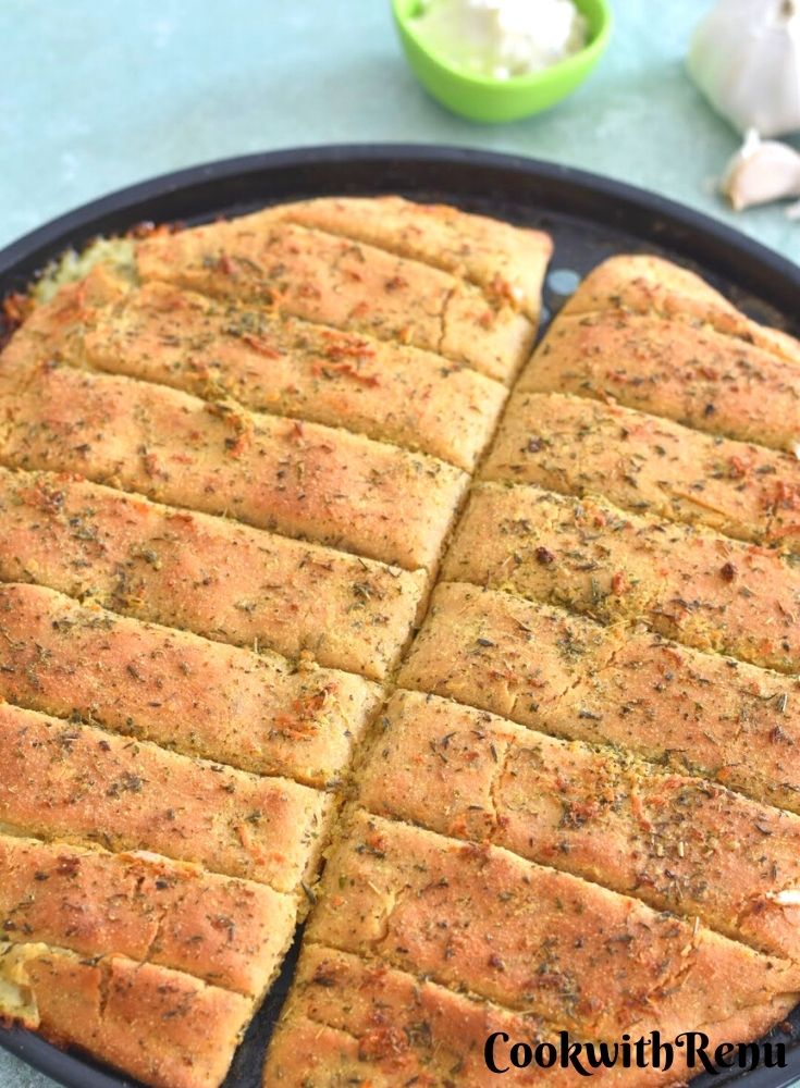 Dominos Style Cheese Garlic Breadsticks on a baking tray with some garlic and mayo on the side