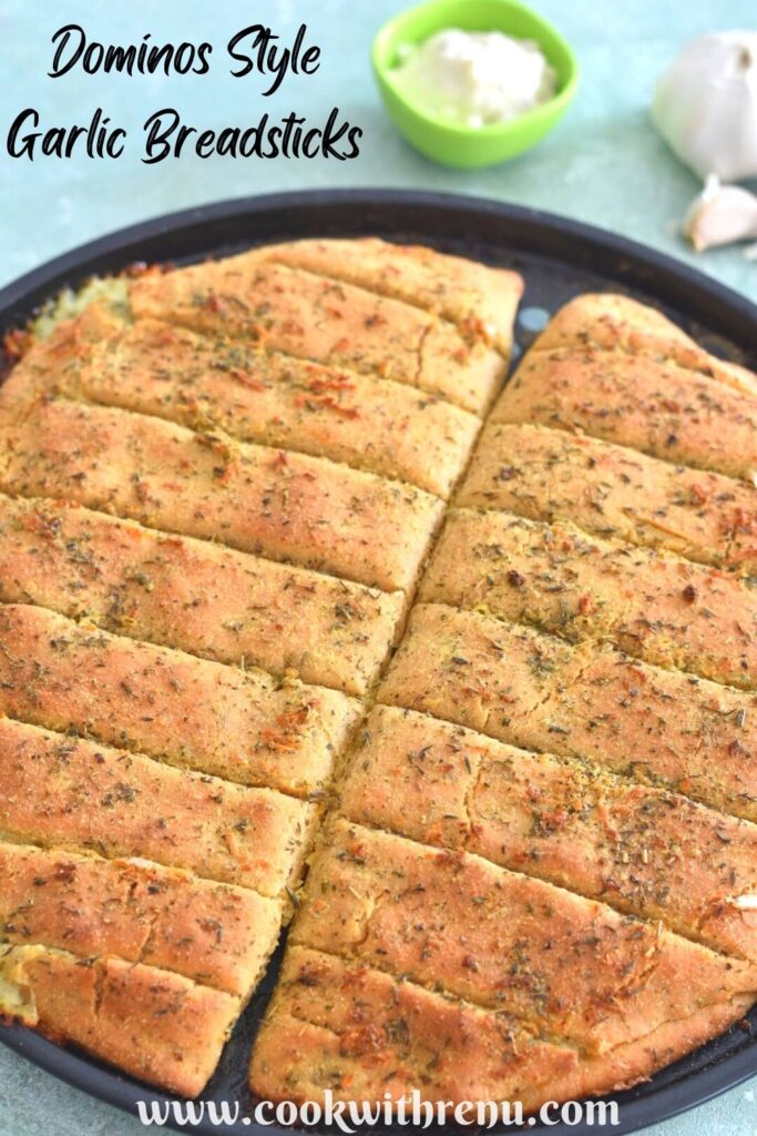 Dominos Style Cheese Garlic Breadsticks on a baking tray with some garlic and mayo on the side