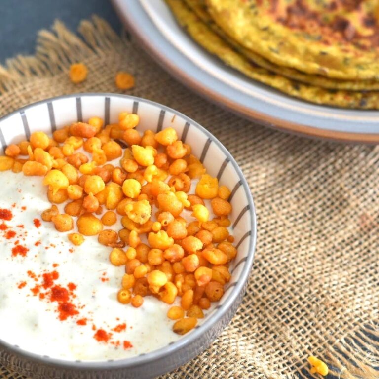 Boondi Raita presented in a bowl with a garish of boondi. Seen are some celery parathas on the side