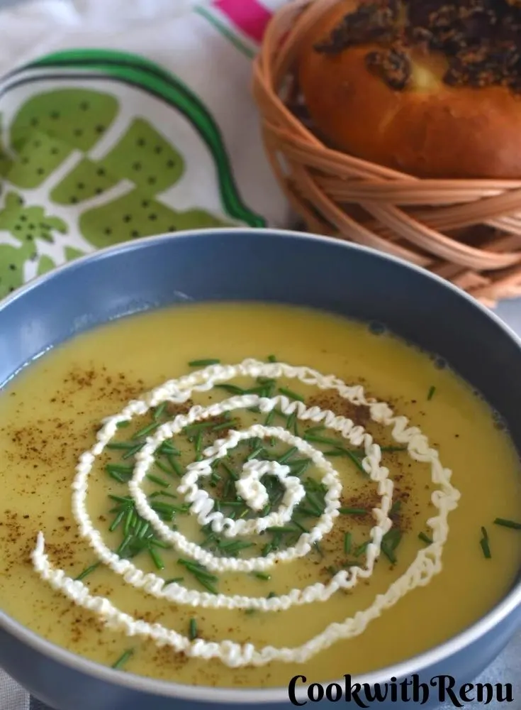 Leek & Potato Soup served in a bowl with a generous garnish of chives and sour cream. Seen in the background is some onion bread.