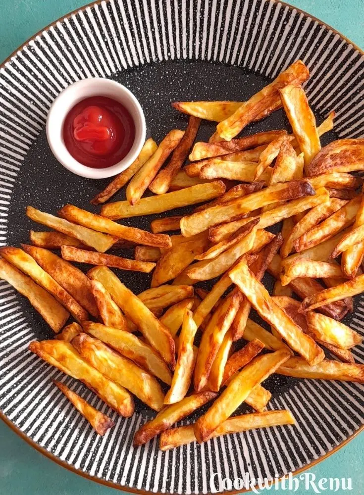 Air fryer French fries served with some tomato ketchup in a black and white plate