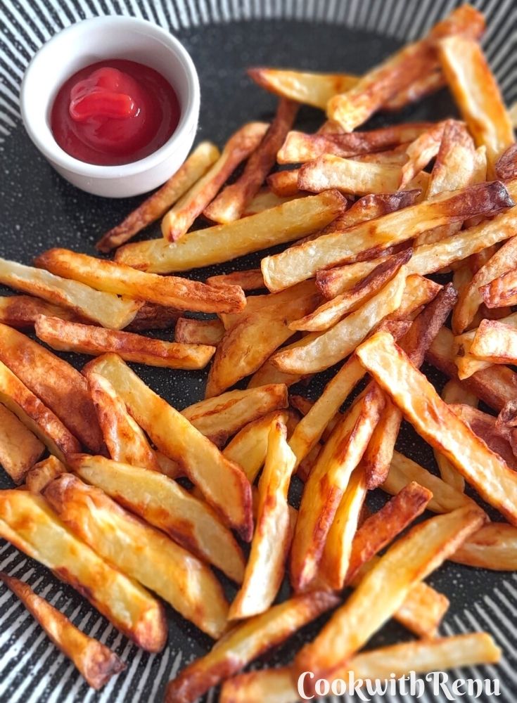 Air fryer French fries served with some tomato ketchup in a black and white plate