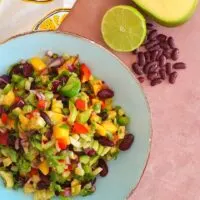 Spicy Avocado Mango Bean Salad served in a blue bowl with golden lining. A cut lime, some beans and mango is seen alongside