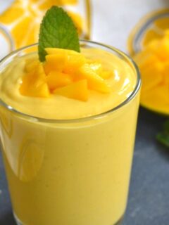 Close up view of Mango Yogurt Smoothie served in a glass, with a garnish of chopped mango and mint