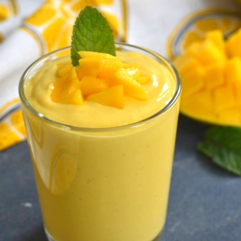 Close up view of Mango Yogurt Smoothie served in a glass, with a garnish of chopped mango and mint