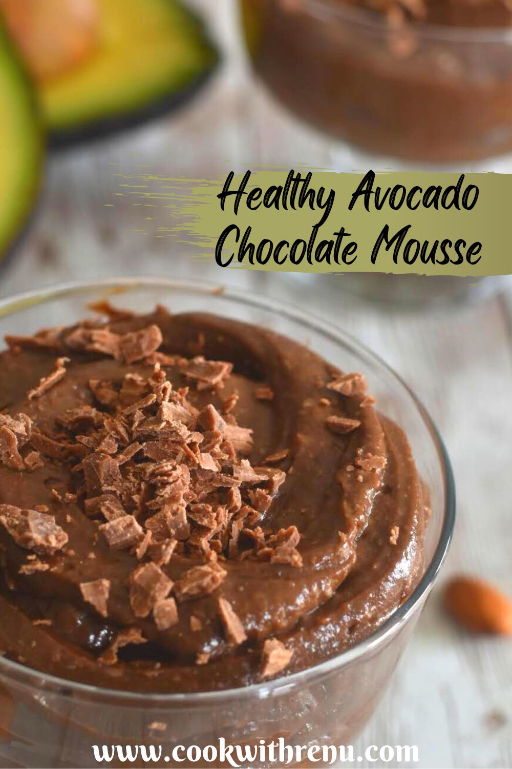 Avocado chocolate mousse served in a glass bowl with a garnish of chopped chocolate. Seen in the background are some cut avocado.