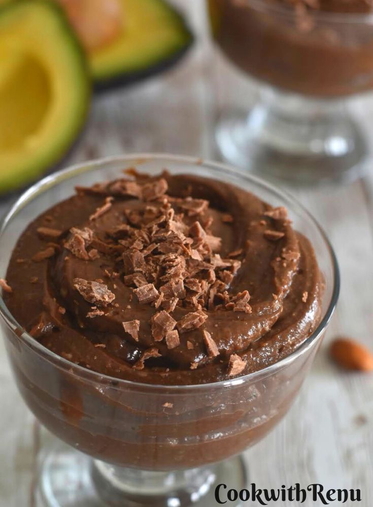 Avocado chocolate mousse served in a glass bowl with a garnish of chopped chocolate. Seen in the background are some cut avocado.