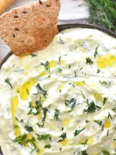 Close up look of Cucumber Dill Tzatziki served in a black bowl along with some baked bread