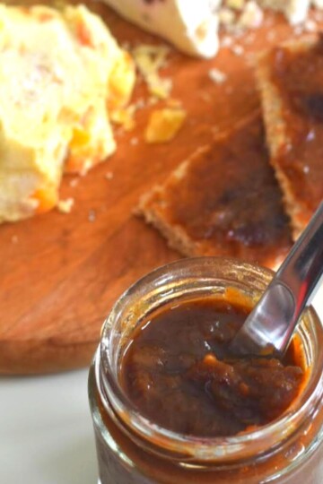 Sweet and Spicy Rhubarb Chutney in a glass jar with some spread on 2 bread slices, served along with some cheese