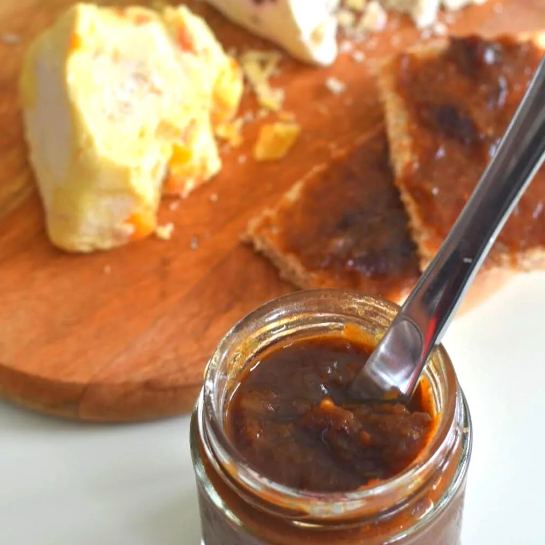 Sweet and Spicy Rhubarb Chutney in a glass jar with some spread on 2 bread slices, served along with some cheese