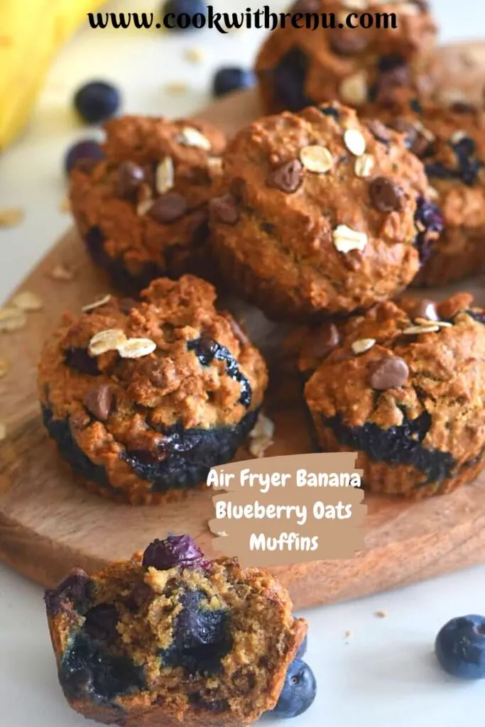 Muffins on a brown cheese board, with a close up look of half muffin in the front and few banana and blueberries in the background