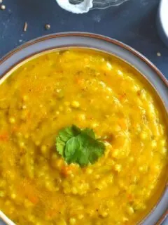 Jowar Moong Dal Khichd served in a grey bowl, with curd and some papad
