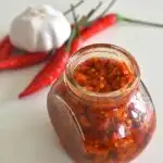 Harrisa Paste in a glass jar. Seen in the background are some red chilly and onion