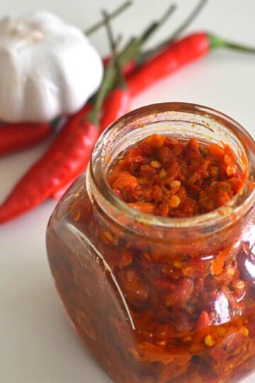 Harrisa Paste in a glass jar. Seen in the background are some red chilly and onion
