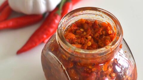 Harrisa Paste in a glass jar. Seen in the background are some red chilly and onion