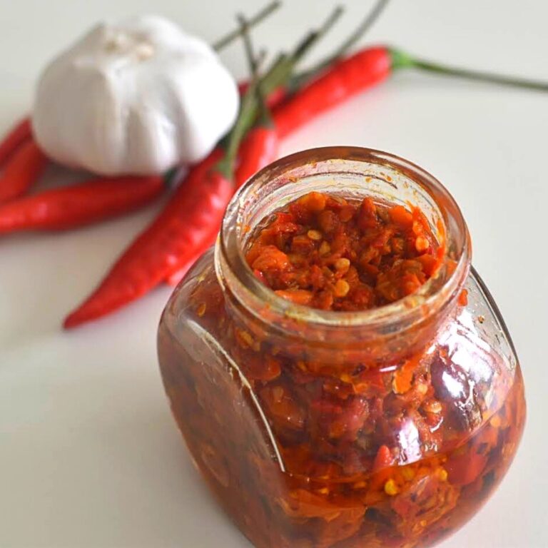 Harrisa Paste in a glass jar. Seen in the background are some red chilly and onion