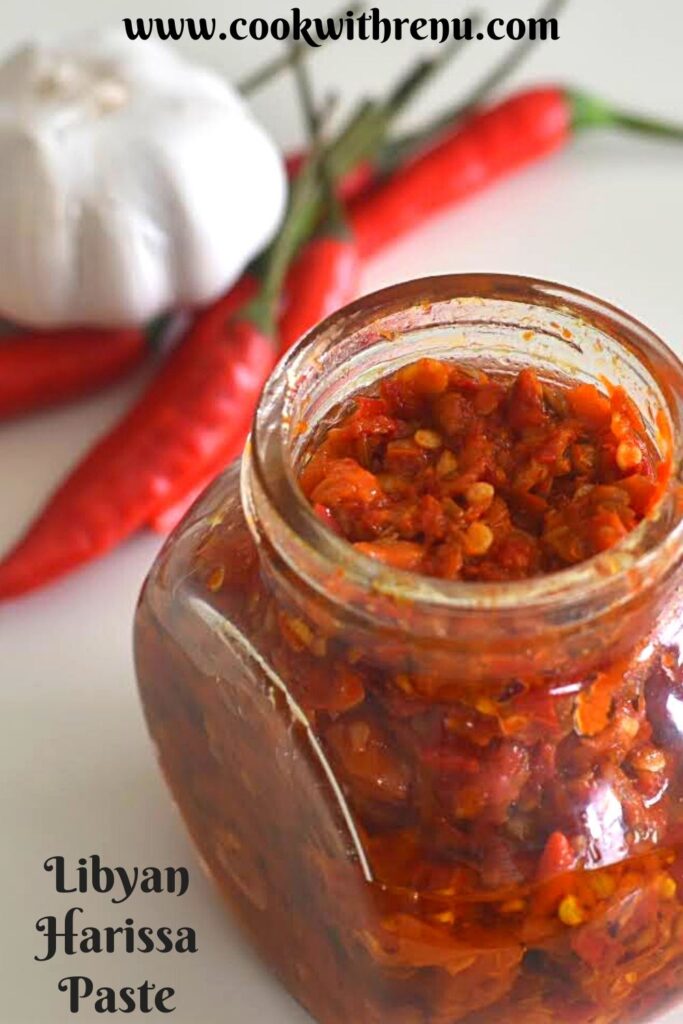 Harrisa Paste in a glass jar. Seen in the background are some red chilly and onion