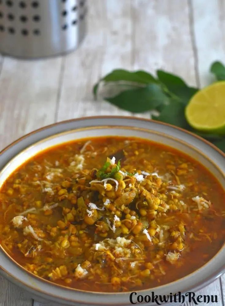 Close up look of Mugachi Usal or Sprouted moong curry in a white bowl. Seen along are some curry leaves and a wedge of lemon
