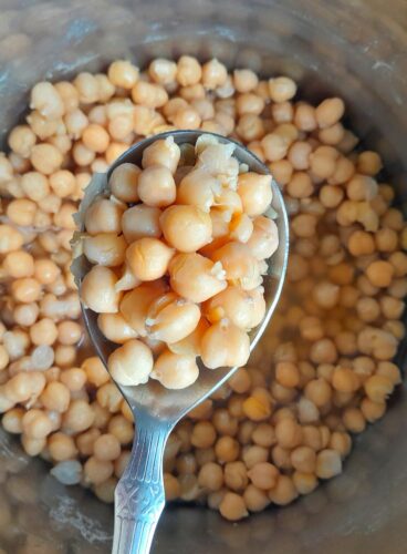 Cooked chickpeas seen in a spoon on top of an Instant pot vessel with chickpeas in it