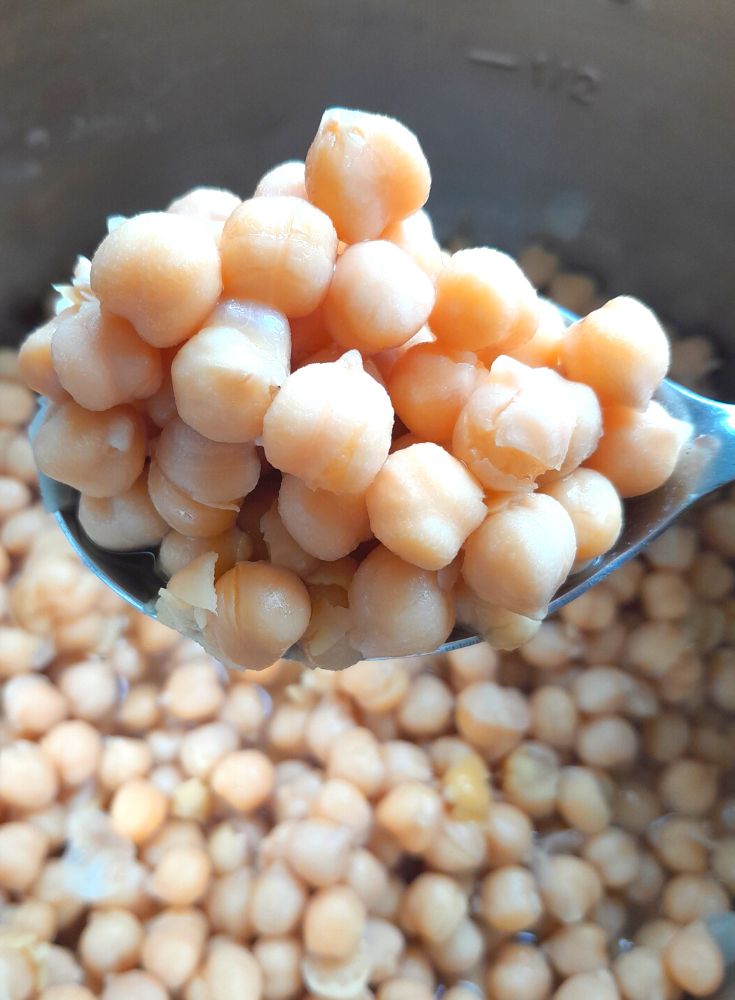 Cooked chickpeas seen in a spoon on top of an Instant pot vessel with chickpeas in it