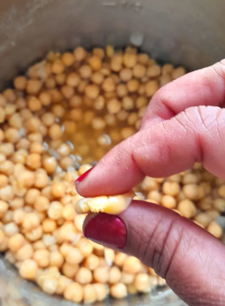 Chickpeas being pressed in between finger and thumb to show the texture of the chickpeas cooked in Instant Pot or Pressure Cooker.