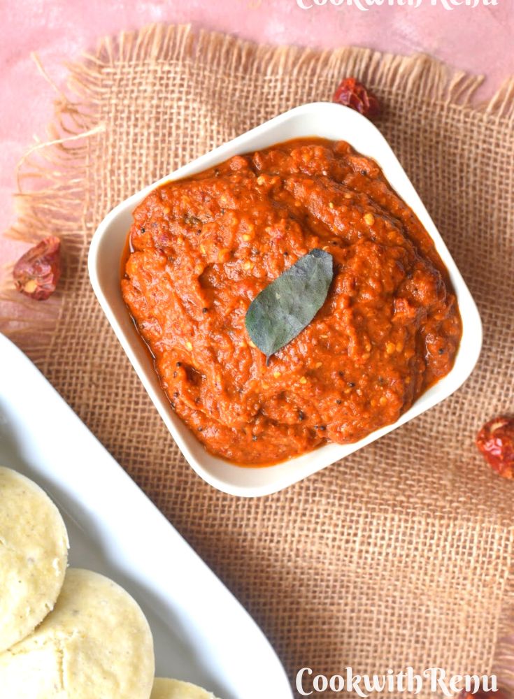 Close up look of Spicy Red chili chutney served in a bowl along with some millet idlis on the side.