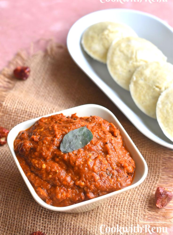 Close up look of Spicy Red chili chutney served in a bowl along with some millet idlis on the side.