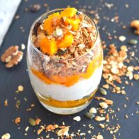 Mango Parfait served in a glass with some granola sprinkled on the sides on a black board.