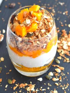 Mango Parfait served in a glass with some granola sprinkled on the sides on a black board.