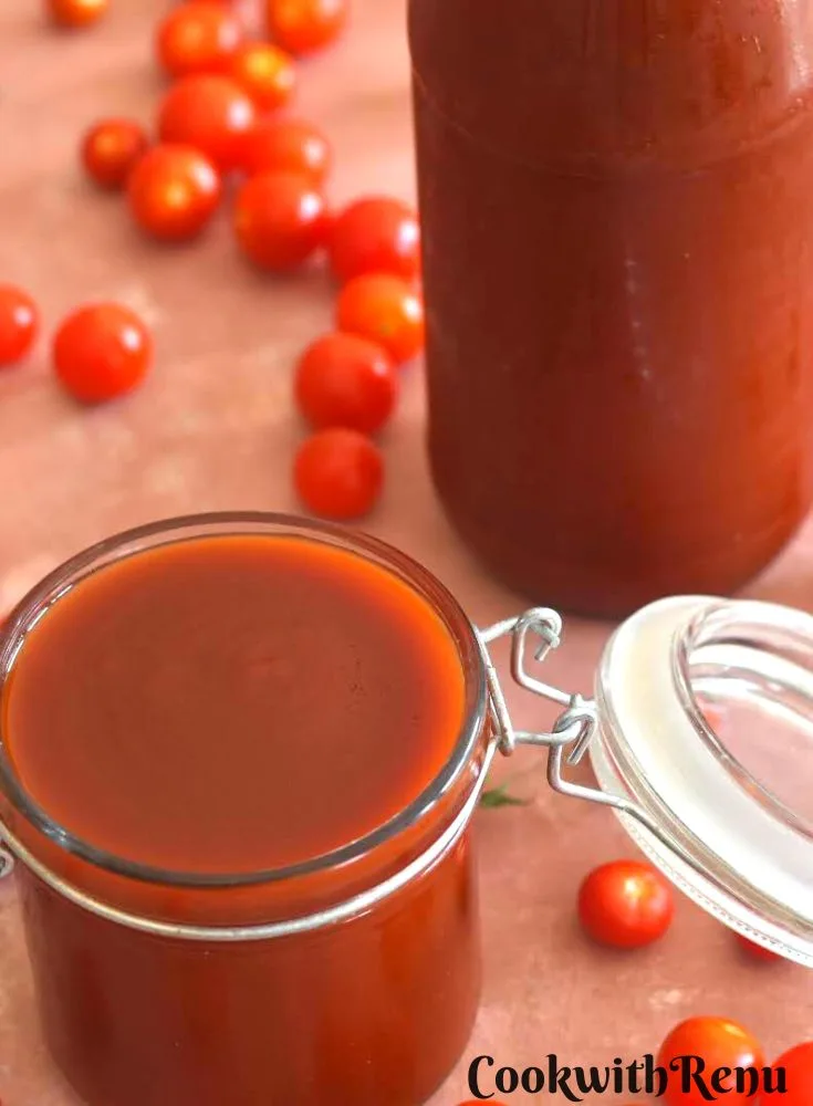 Tomato ketchup in a glass jar and a glass bottle with some cherry tomaotes lying all over.