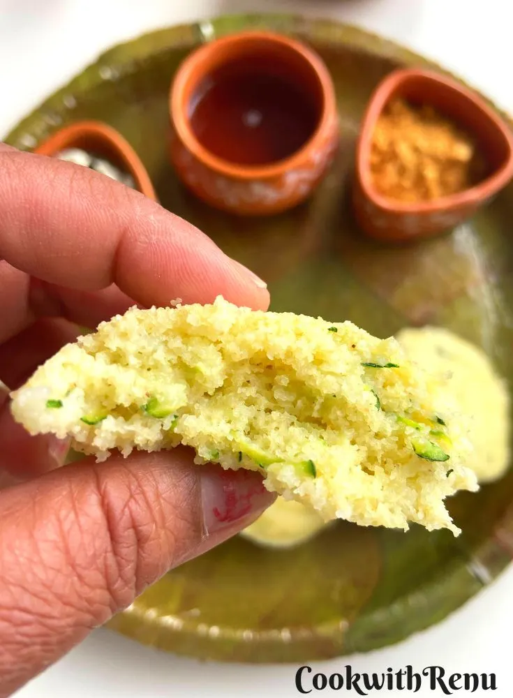 Close up view of Inside Texture of Rava Zucchini Idli seen, with an Idli plate in background.