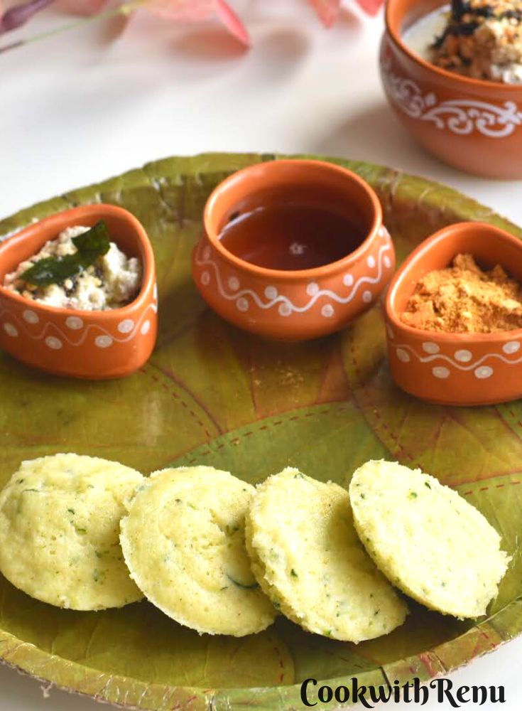 Close up view of Instant Vegetable Rava Idli served in a green plate, with chutneys, podi and sesame oil.