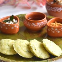 Close up view of Instant Vegetable Rava Idli served in a green plate, with chutneys, podi and sesame oil.