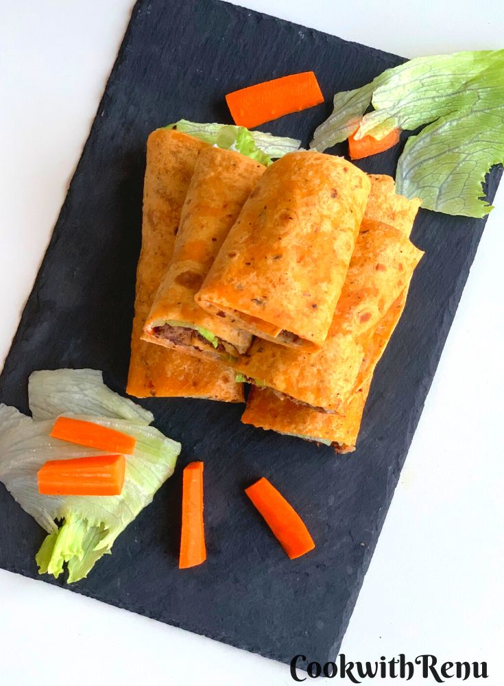Top view of Kidney Bean Patties Wraps arranged on a black cheese board with some carrots and lettuce seen on the side.