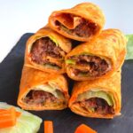 Kidney Bean Patties Wraps arranged on a black cheese board with some carrots and lettuce seen on the side.